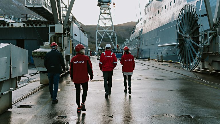 Fire personer iført røde jakker med VARD-logo på fotografert bakfra mens de går på kaia ved siden av KV Jan Mayen