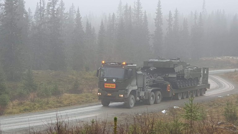 Semitrailer med trekkvogn med stridsvogn på kjører på en grusvei i skogen i tåke