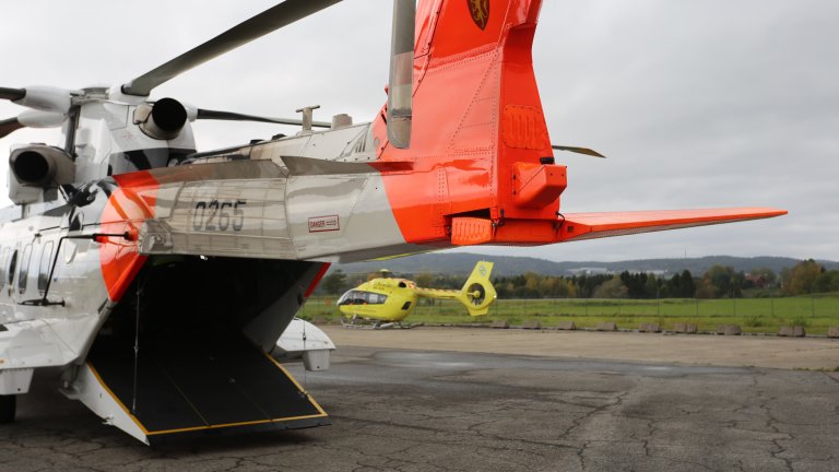 Redningshelikopter med lemmen nede parkert på flystripe med luftambulanse i bakgrunnen