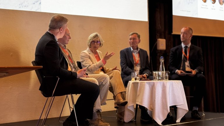 Fem personer deltar i en paneldebatt. En kvinne i lyse klær snakker.