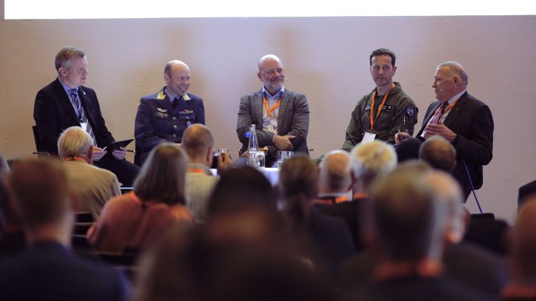 Fem menn i en paneldebatt foran et publikum, hvor to er i militæruniform og resten i sivile klær.