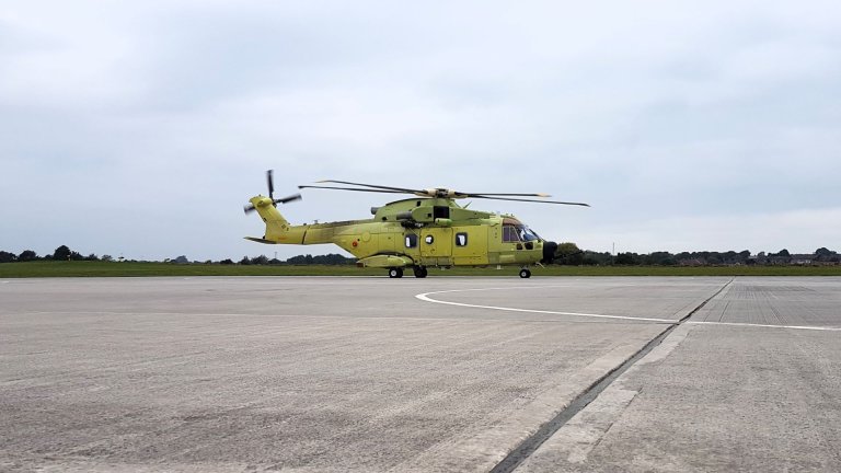 Et helikopter i gulgrønn farge står på bakken ved en flyplass