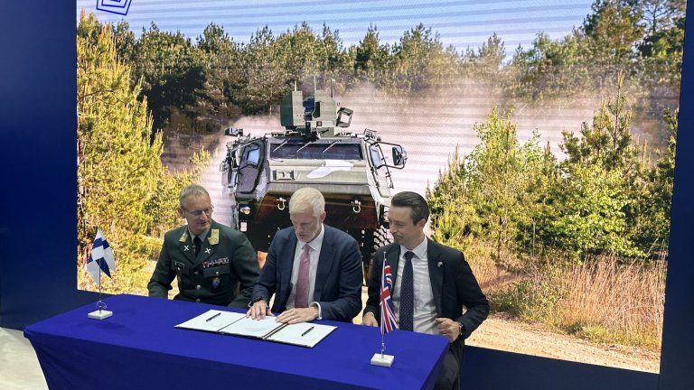 Tre menn signerer dokumenter foran bilde av militært kjøretøy i skogen.