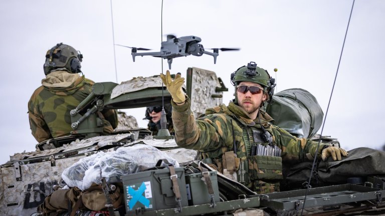 Soldater på et militært kjøretøy med en drone i luften.