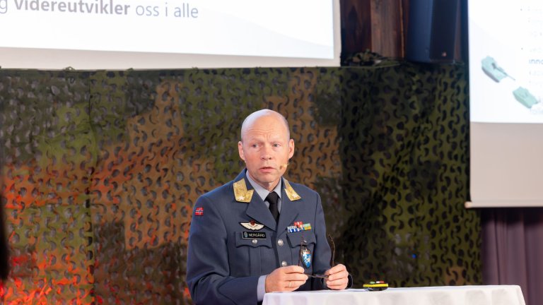 Mann iført uniform snakker til forsamling fra scene