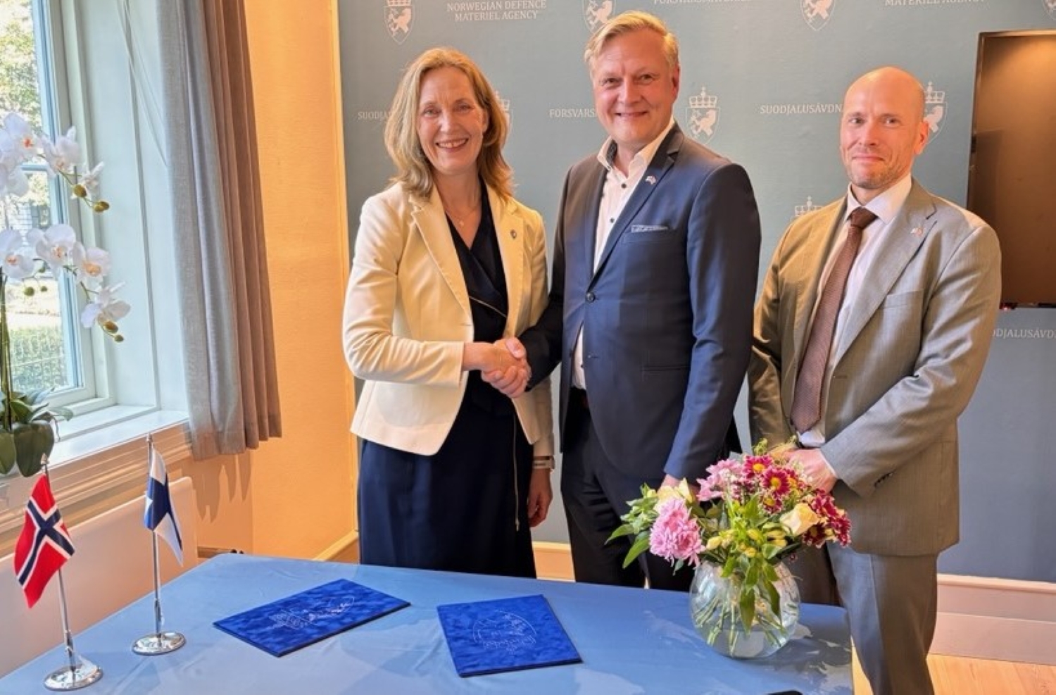 En kvinne og to menn ved et signeringsbord med norsk og finsk flagg