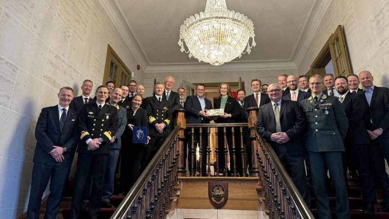 Gruppebilde av uniformert og sivilt personell samlet i en trapp under en lysekrone.