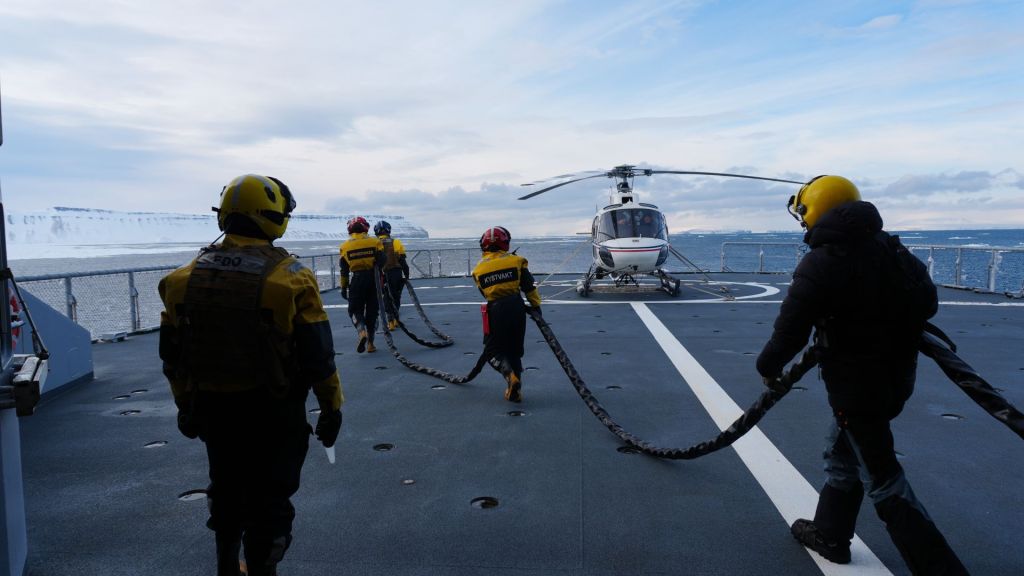 Helikopteret har landet på KV Svalbard for lading av batteri og startstrøm. Isbjørnforskerne har observert flere isbjørn de ønsker å sjekke ut. Flydekkspersonell drar strømkabelen til helikopteret slik at det kan gjøres klart til en tur til. Foto: Forsvarsmateriell  
