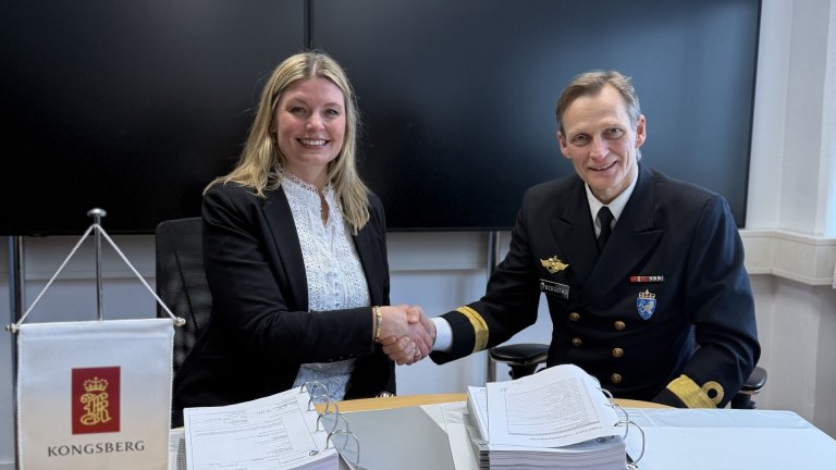 Mann og  kvinne har hverandre i hånden ved bord med permer.