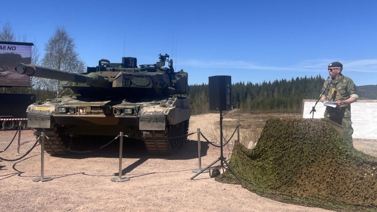 Mann i uniform taler ved siden av stridsvogn