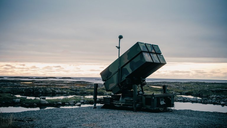 Utskytingsenhet i kamuflasjefarger står oppreist foran en skjærgård ut mot havet