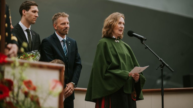 Woman in Norwegian national costume speaking into a microphone