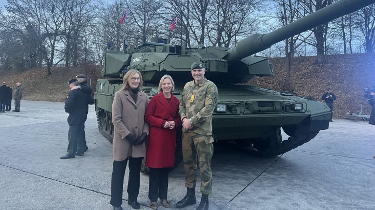 Three smiling people standing in front of a battle tank