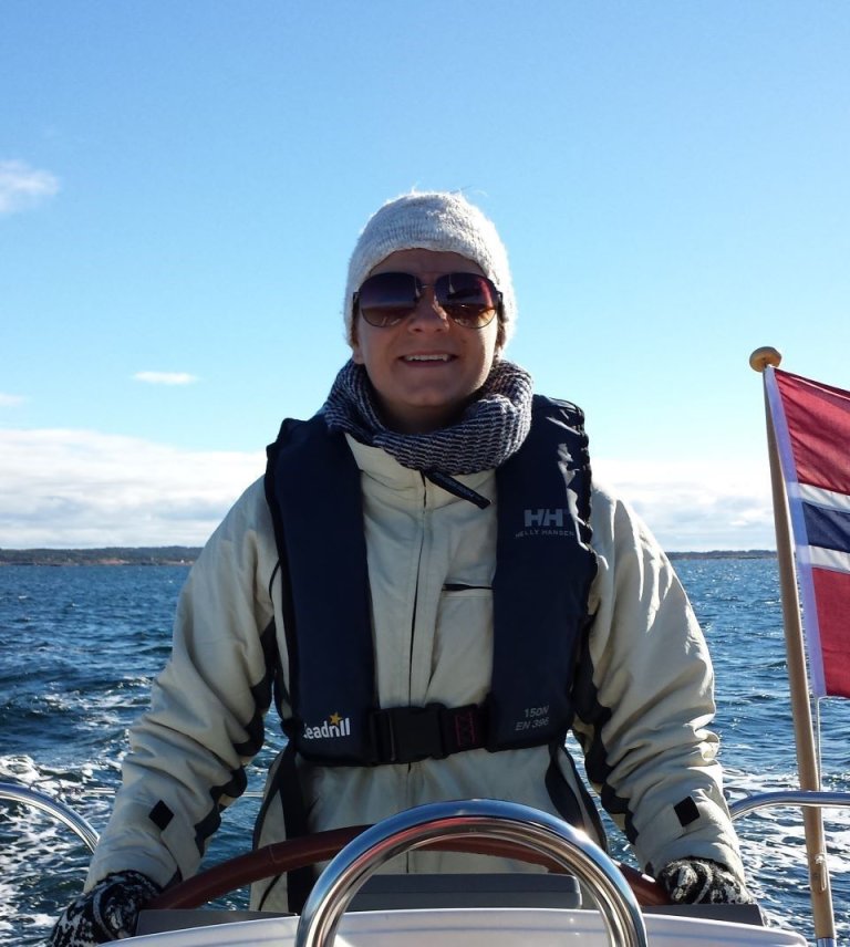 Smilende kvinne som kjører båt ikledd solbriller og lue